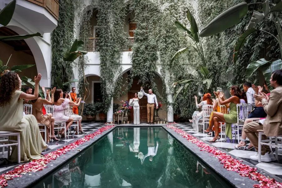 Couple celebrating at a riad pool ceremony framed by hanging greenery - riad wedding Marrakech