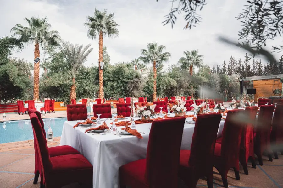 Poolside reception table with red velvet chairs beneath palm trees - wedding venue Marrakech