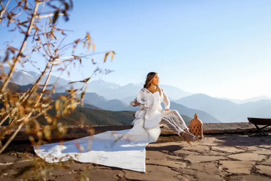 Bride seated on a terrace with the snow-capped Atlas Mountains behind - destination wedding photographer Morocco