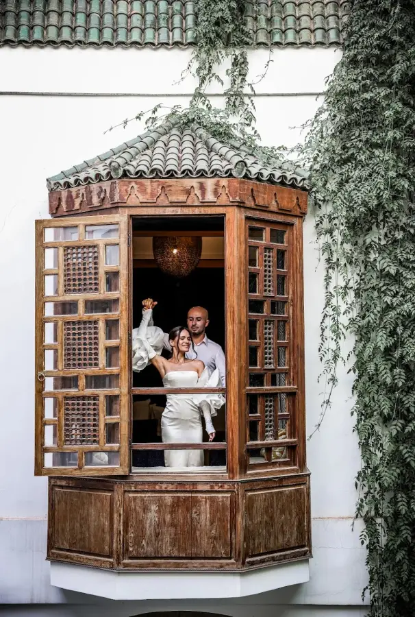 Couple framed in a carved wooden riad window surrounded by ivy - riad wedding photography Marrakech