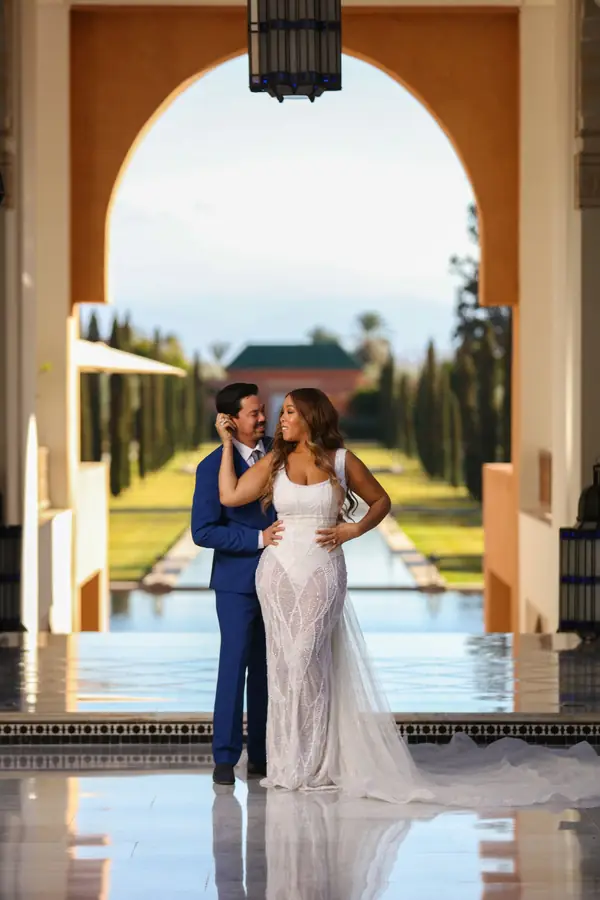 Bride and groom beside a long reflecting pool framed by a Moorish arch - luxury wedding photography Marrakech
