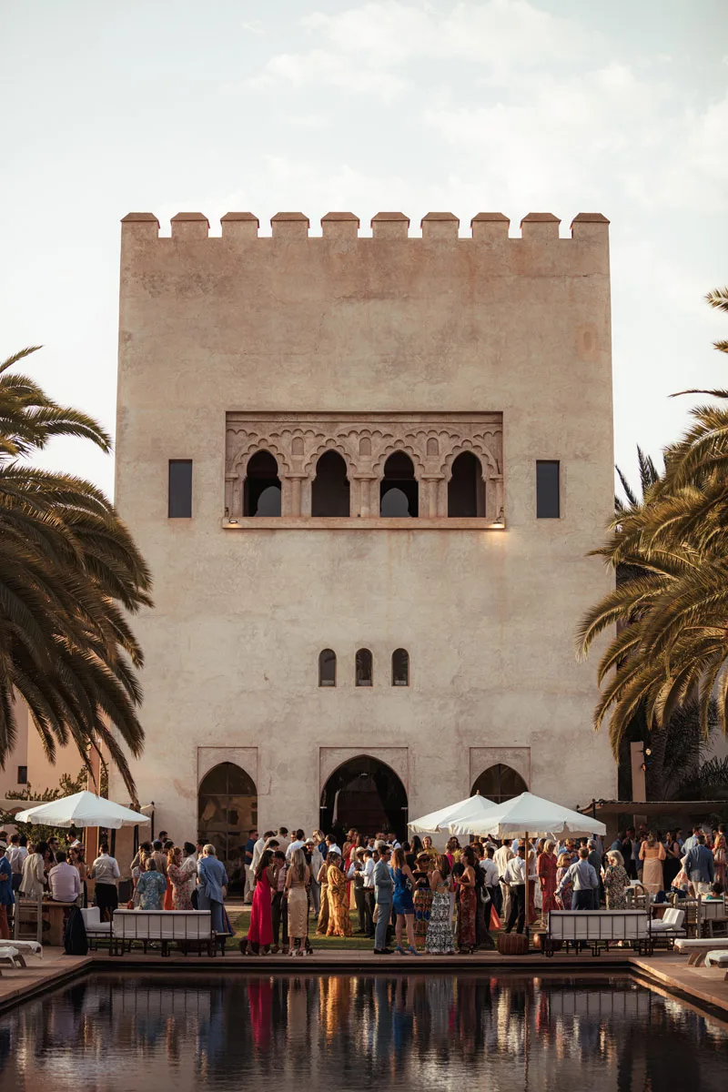 Guests gathered by the pool in front of a kasbah tower at golden hour - wedding venue Marrakech